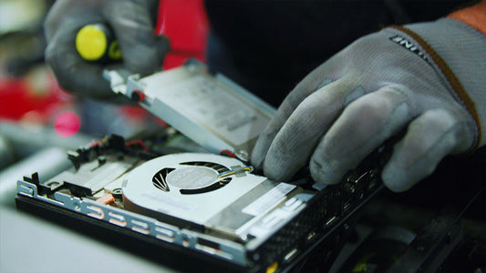 Electronics recycling warehouse worker wearing gloves to unscrew a hard drive